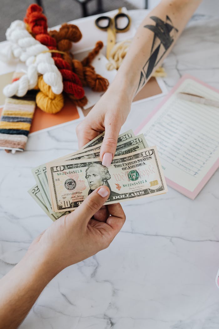 why-choose-us Hands exchanging US dollars on a table with crafting supplies, highlighting financial transactions.