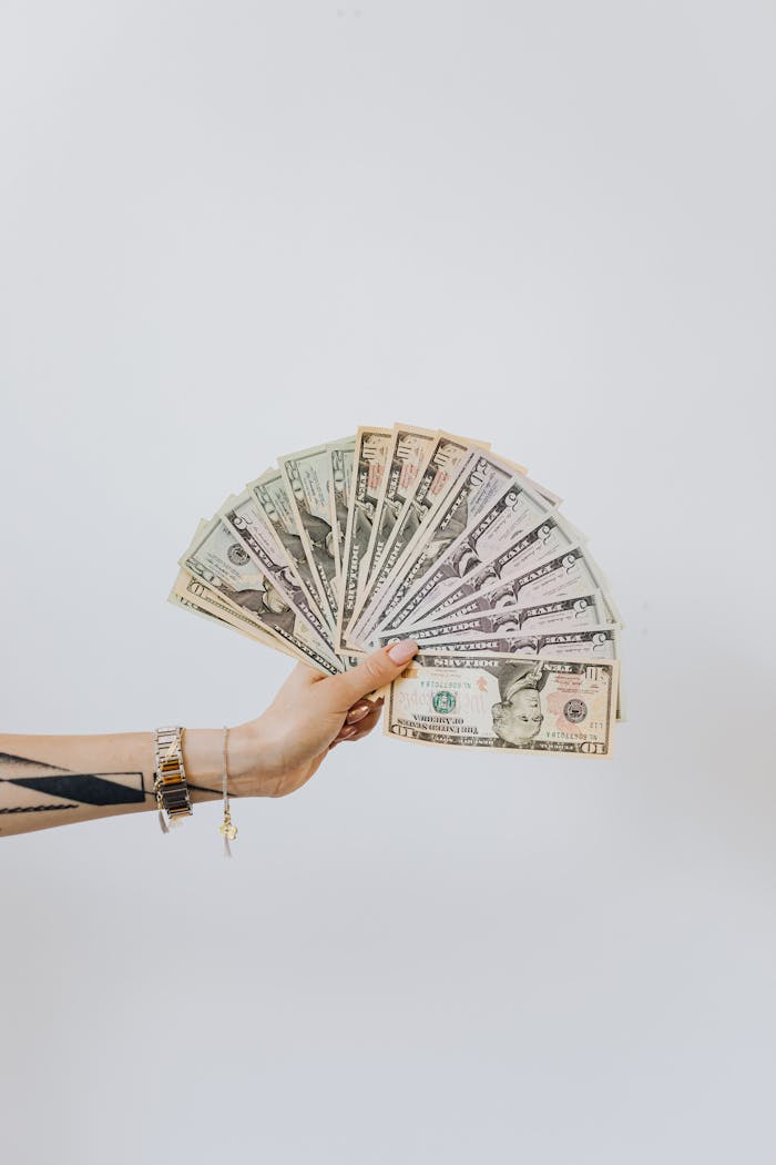 Close-up of a hand displaying fanned out US dollar bills against a white background.