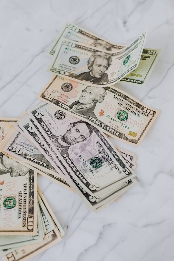 hero-img-01 Crisp US dollar bills scattered on a marble surface, symbolizing wealth and finance.